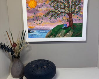 May include: A framed painting depicts a person sitting under a tree on a grassy cliff overlooking a blue ocean with a bright yellow sun in a pink and purple sky. Beside it sits a dark gray steel tongue drum with numbered notes and two mallets.