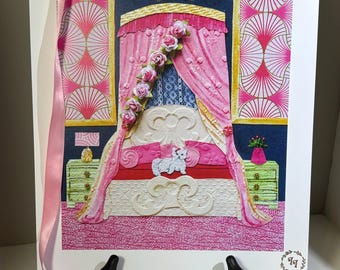 May include: A framed artwork depicts a pink and white bedroom scene. The bed has a canopy with pink drapes and rose accents. A white cat rests on the red and pink bedding. The artwork is displayed on a black easel with pink ribbon.