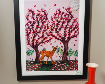 May include: Framed art print featuring a deer standing between two trees with red and pink leaves. The artwork is set against a light pink background with falling leaves. A red vase with a white rim sits in front of the artwork.