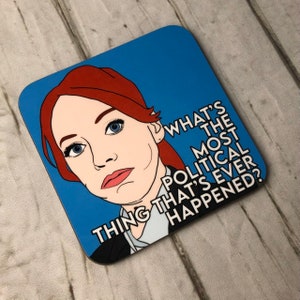 May include: A blue and red illustrated coaster featuring a woman with red hair and the text "What's the most political thing that's ever happened?"