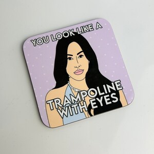 Peut inclure: Un dessous de verre violet &agrave; pois blancs avec une illustration de dessin anim&eacute; d'une femme aux longs cheveux noirs et le texte "You look like a trampoline with eyes."