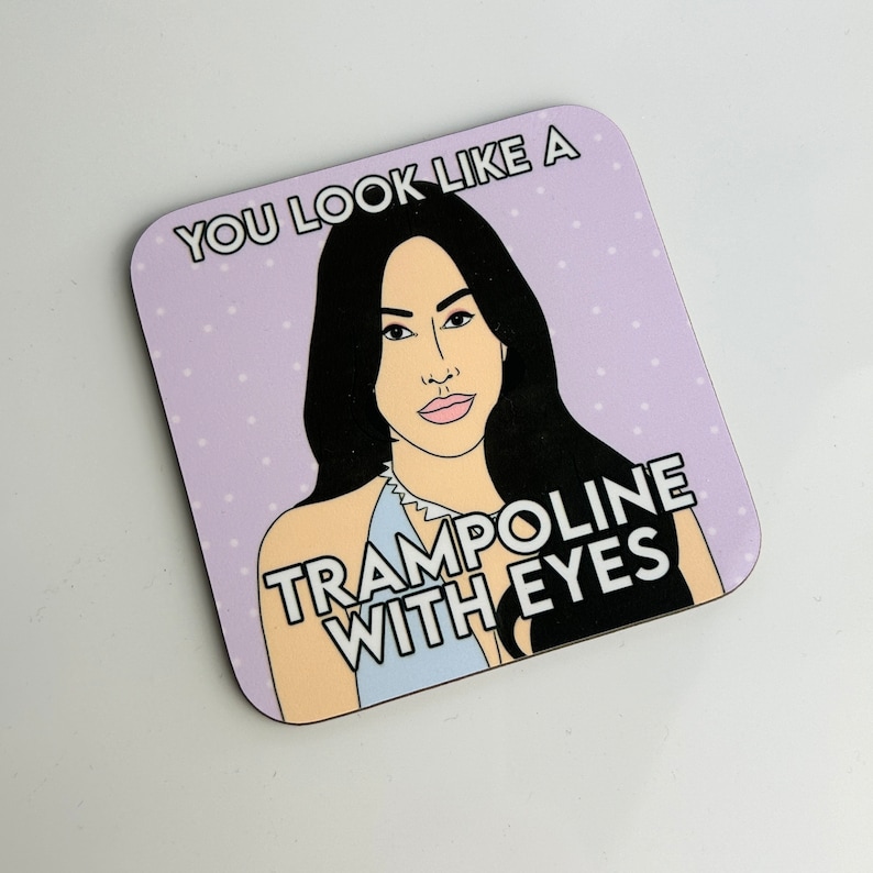 Peut inclure: Un dessous de verre violet &agrave; pois blancs avec une illustration de dessin anim&eacute; d'une femme aux longs cheveux noirs et le texte "You look like a trampoline with eyes."