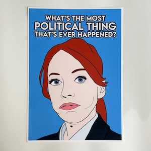May include: A pop art style print featuring a woman with red hair and blue eyes against a blue background. The text at the top reads, "WHAT'S THE MOST POLITICAL THING THAT'S EVER HAPPENED?"