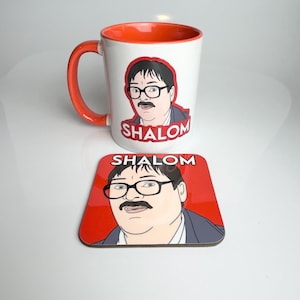 May include: A white ceramic mug with an orange rim and a cartoon image of a man with glasses and a moustache. The mug has the word "SHALOM" printed on it in red. A matching coaster with the same image and text is also shown.