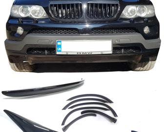May include: A black BMW X5 SUV with a black grille and a license plate that says "UA". The car is surrounded by a set of black plastic trim pieces for the car's body.