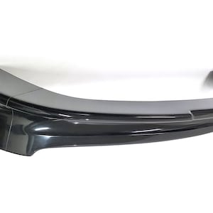 Puede incluir: Un difusor trasero de pl&aacute;stico negro para un coche. El difusor tiene una forma curva y un acabado liso.