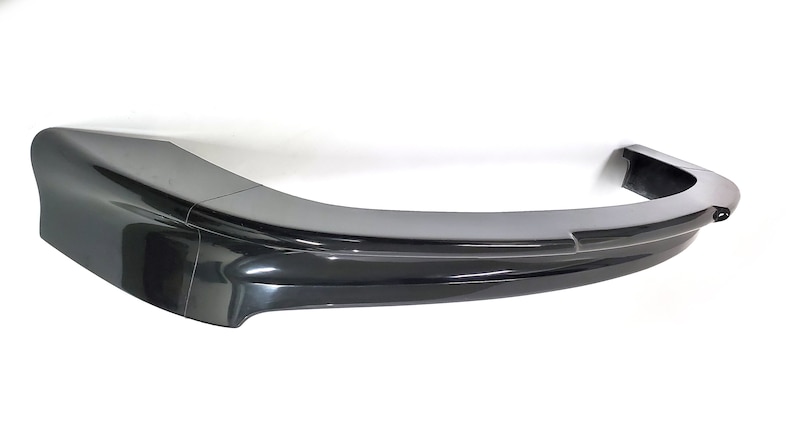 Puede incluir: Un difusor trasero de pl&aacute;stico negro para un coche. El difusor tiene una forma curva y un acabado liso.