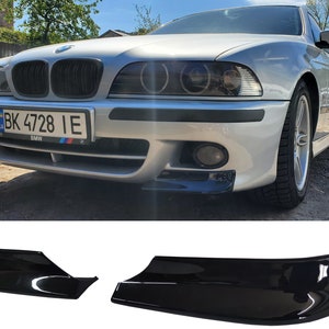 May include: A black plastic car spoiler with a glossy finish. The spoiler is designed to fit the front bumper of a car. The spoiler is shown in two pieces, one for each side of the bumper.