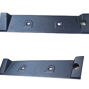 Könnte beinhalten: Zwei schwarze Kunststoffplatten mit jeweils drei Löchern. Die Platten sind rechteckig und haben eine leicht strukturierte Oberfläche.