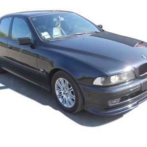 Puede incluir: Un sed&aacute;n BMW Serie 5 negro con una parrilla cromada y llantas de aleaci&oacute;n plateadas. El coche est&aacute; aparcado sobre un fondo blanco.