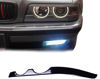 Könnte beinhalten: Nahaufnahme eines grauen Autos mit hellweißen Halo-Scheinwerfern und einem roten Akzent am Kühlergrill. Darunter zwei schwarze, gebogene Autozubehörteile.