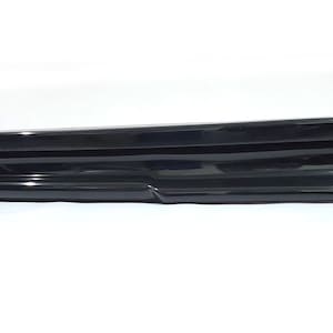 Puede incluir: Un aler&oacute;n de coche de pl&aacute;stico negro con un dise&ntilde;o liso y curvo. El aler&oacute;n tiene un labio ligeramente elevado en el borde inferior.
