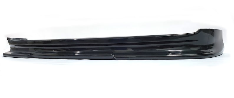 Puede incluir: Un aler&oacute;n de coche de pl&aacute;stico negro con un dise&ntilde;o liso y curvo. El aler&oacute;n tiene un labio ligeramente elevado en el borde inferior.