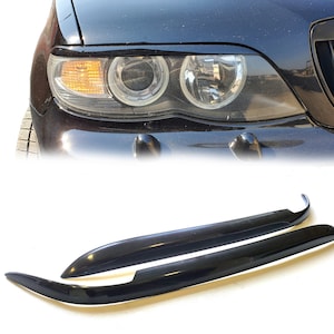 Może przedstawiać: Para czarnych plastikowych listew ozdobnych do reflektorów samochodowych. Listwy są zaprojektowane tak, aby pasowały nad reflektory i nadać samochodowi bardziej agresywny wygląd.