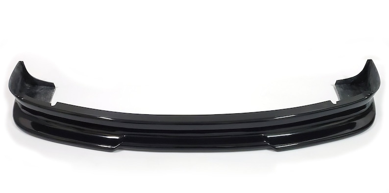 Puede incluir: Un aler&oacute;n de parachoques delantero de coche negro con un acabado liso y brillante. El aler&oacute;n tiene un dise&ntilde;o de tres piezas con una forma curva.