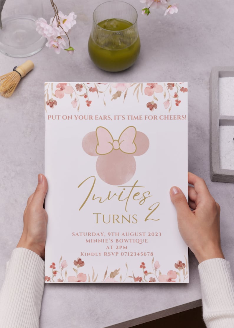 May include: A pink and gold invitation card with a floral border. The card features a cartoon image of Minnie Mouse and the text "Invites Turns 2". The invitation details a party on Saturday, August 9th, 2023 at 2pm at Minnie's Bowtique. The card also includes the text "Kindly RSVP 0712345678".