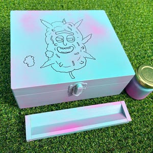 Può includere: Un set composto da una scatola di legno, un vassoio e un barattolo. La scatola e il vassoio sono dipinti con un gradiente di rosa e blu e presentano un'illustrazione di un personaggio dei cartoni animati nero. Il barattolo ha un coperchio dorato.
