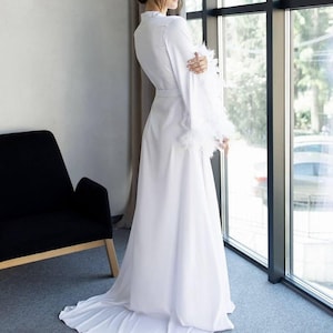 Bata de novia de seda blanca con cola y mangas adornadas con plumas: elegante atuendo para bodas de mañana