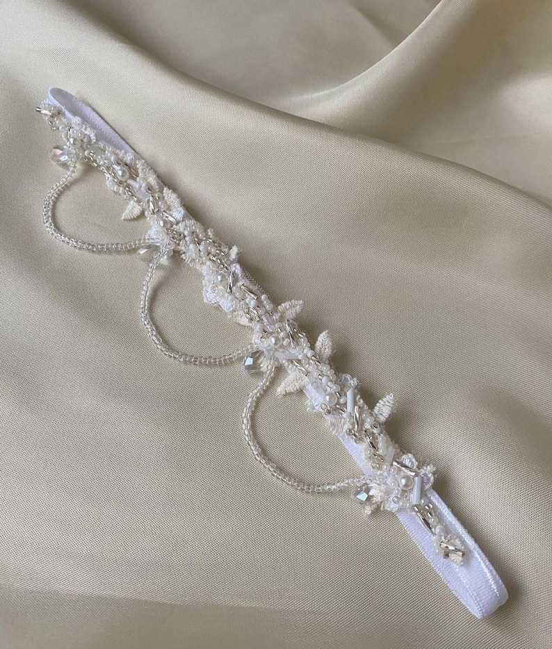 May include: White bridal garter featuring delicate beaded lace and pearl embellishments. The garter has a white elastic band and a decorative beaded design.