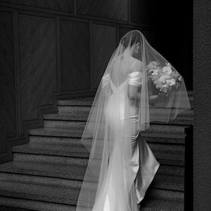 May include: A bride in a white wedding dress and veil walks down a set of stairs, holding a bouquet of white flowers.