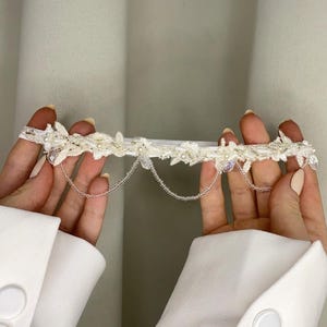 May include: White bridal garter with delicate lace and pearl embellishments, featuring a beaded chain detail.