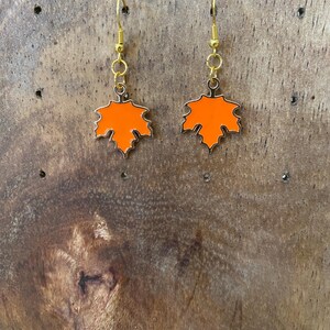 May include: A pair of gold dangle earrings with orange maple leaf charms.