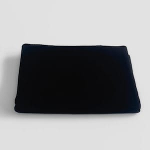 May include: A folded, rectangular black fabric, possibly a blanket or throw, is centered against a plain white background. The fabric appears soft and plush, with a slightly textured surface. The edges are neatly folded, creating a clean, minimalist aesthetic.