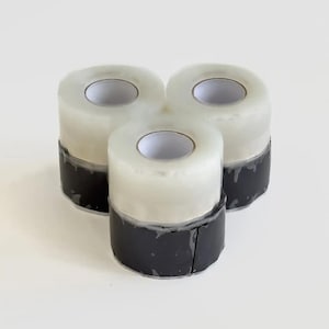 May include: Three rolls of clear tape with black bases are arranged in a triangular pattern. The tape rolls have a white core and a transparent, glossy outer layer. The black bases appear to be made of a flexible material.
