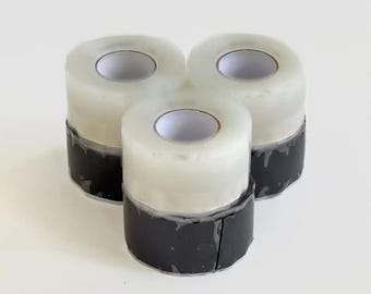 May include: Three rolls of clear tape with black bases are arranged in a triangular pattern. The tape rolls have a white core and a transparent, glossy outer layer. The black bases appear to be made of a flexible material.
