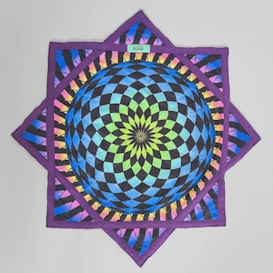 May include: A geometric quilt with a central sphere in a checkered pattern of blue, green, and black. The sphere is set within a star-shaped purple border, with a rainbow design. The text "INNER FLOW" is visible.