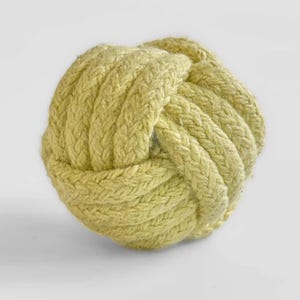 May include: A decorative, round knot made of thick, light green rope. The rope is tightly woven, creating a textured surface. The knot is a nautical-themed decorative item, perfect for coastal decor.