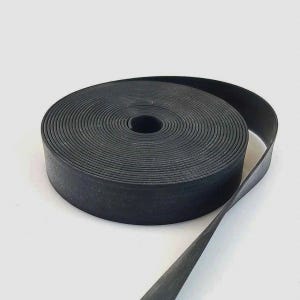 May include: A roll of black, textured tape, unspooled at the end. The tape is tightly wound, revealing a central hole. The material appears to be rubber or a similar flexible substance. The background is plain white.