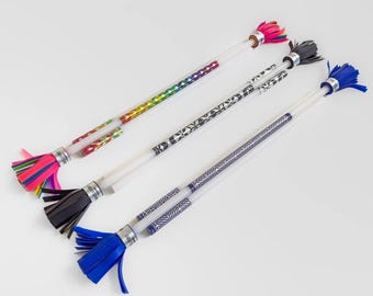 May include: Four juggling sticks with clear plastic shafts and patterned designs. Each stick has a different coloured tassel at the end: pink, black, blue, and a rainbow of colours. The sticks are arranged diagonally on a white surface.
