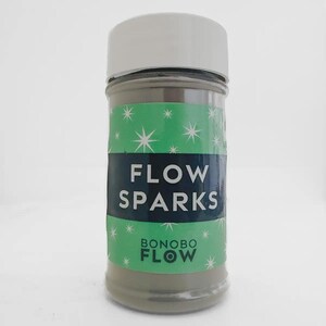 May include: A clear glass jar with a white lid, filled with a gray powder. The jar has a green label with white starbursts and the words "FLOW SPARKS" in white and "BONOBO FLOW" in green.