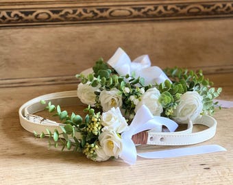 Può includere: Due collari per cani in pelle bianca con nastro di raso bianco e fiori bianchi con foglie verdi.