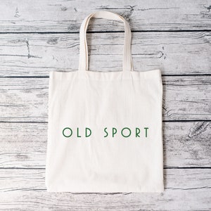 K&ouml;nnte beinhalten: Eine wei&szlig;e Stofftasche mit dem Text "OLD SPORT" in Gr&uuml;n auf der Vorderseite.