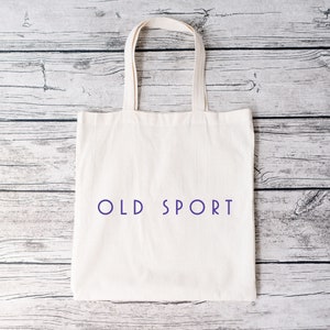 K&ouml;nnte beinhalten: Wei&szlig;e Stofftasche mit dem Aufdruck "OLD SPORT" in Lila auf der Vorderseite.