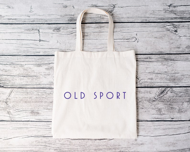 K&ouml;nnte beinhalten: Wei&szlig;e Stofftasche mit dem Aufdruck "OLD SPORT" in Lila auf der Vorderseite.