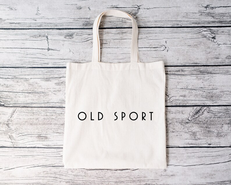 K&ouml;nnte beinhalten: Eine wei&szlig;e Canvas-Tragetasche mit schwarzen Henkeln und dem Text "OLD SPORT" in Schwarz auf der Vorderseite.