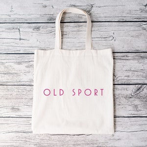 K&ouml;nnte beinhalten: Eine wei&szlig;e Canvas-Tragetasche mit dem Aufdruck "OLD SPORT" in Pink auf der Vorderseite.