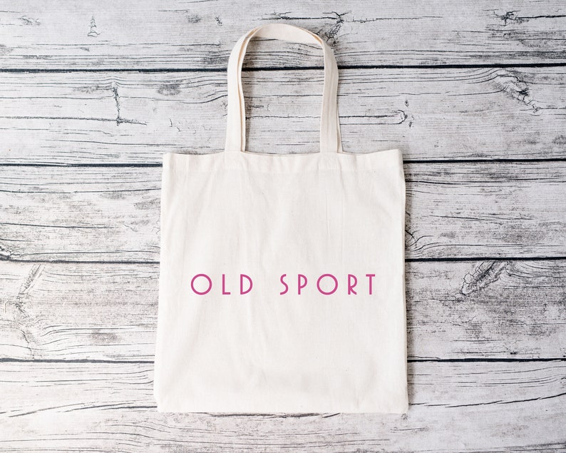 K&ouml;nnte beinhalten: Eine wei&szlig;e Canvas-Tragetasche mit dem Aufdruck "OLD SPORT" in Pink auf der Vorderseite.