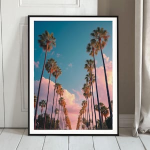 May include: A framed print featuring a scenic view of a palm tree-lined street under a blue sky with pink and white clouds. The tall palm trees create a symmetrical pattern, evoking a sense of tranquility and warmth.