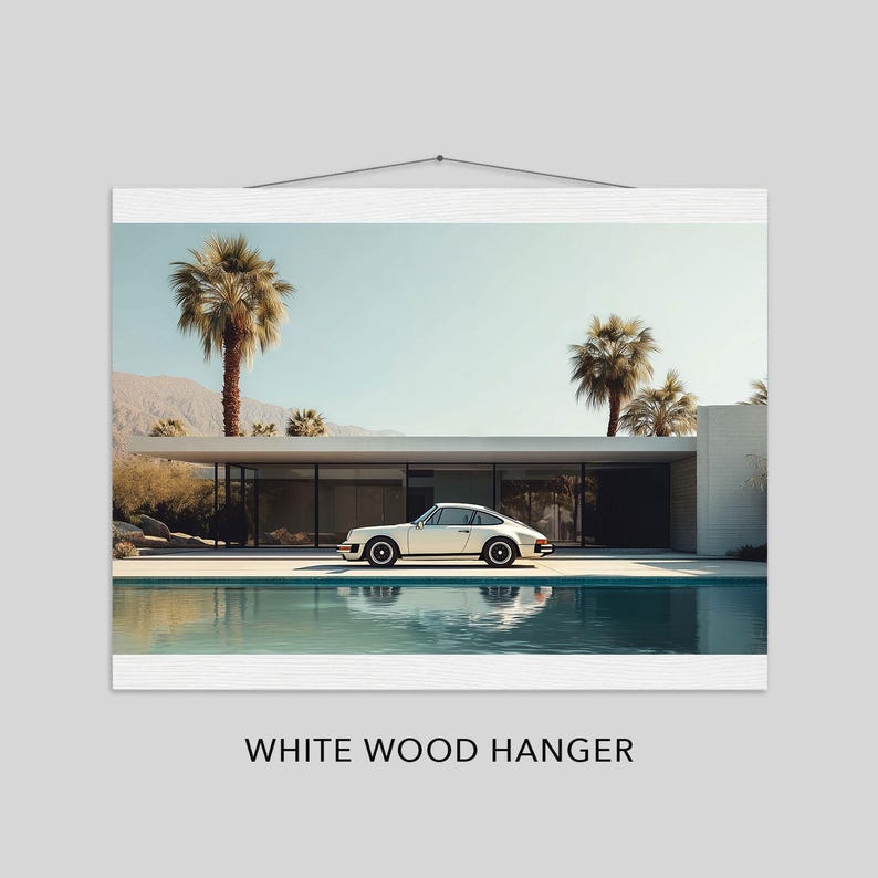 May include: A framed print featuring a white sports car parked in front of a modern home with a pool. Palm trees and mountains are in the background under a clear blue sky. The print is displayed with a white wood hanger.