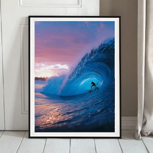 May include: Framed print depicting a surfer inside a large, blue ocean wave. The wave is curling, with a silhouetted surfer riding it. The sky above is a blend of pink and purple, with the sun setting in the distance, creating a dramatic scene.