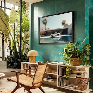 May include: A mid-century modern living room with a framed picture of a white car parked near a pool. The room features a wooden chair with a woven seat, a mushroom-shaped lamp, and a white bookshelf filled with books and plants. The wall is tiled in a teal color.