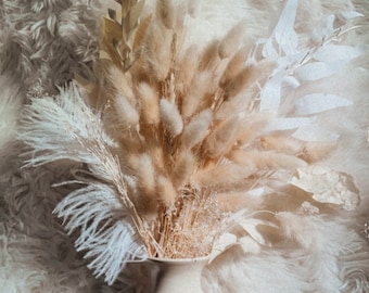 May include: A white ceramic vase filled with dried pampas grass, dried white feathers, and dried eucalyptus leaves.
