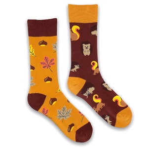 May include: A pair of colourful socks with an autumn theme. The socks feature a brown and orange background with images of squirrels, hedgehogs, leaves, and acorns.