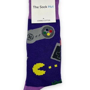 May include: Purple socks with a pattern of retro video game controllers, Pac-Man, and other pixelated graphics. The socks have a tag that says "The Sock Hut" and "Combed Cotton".