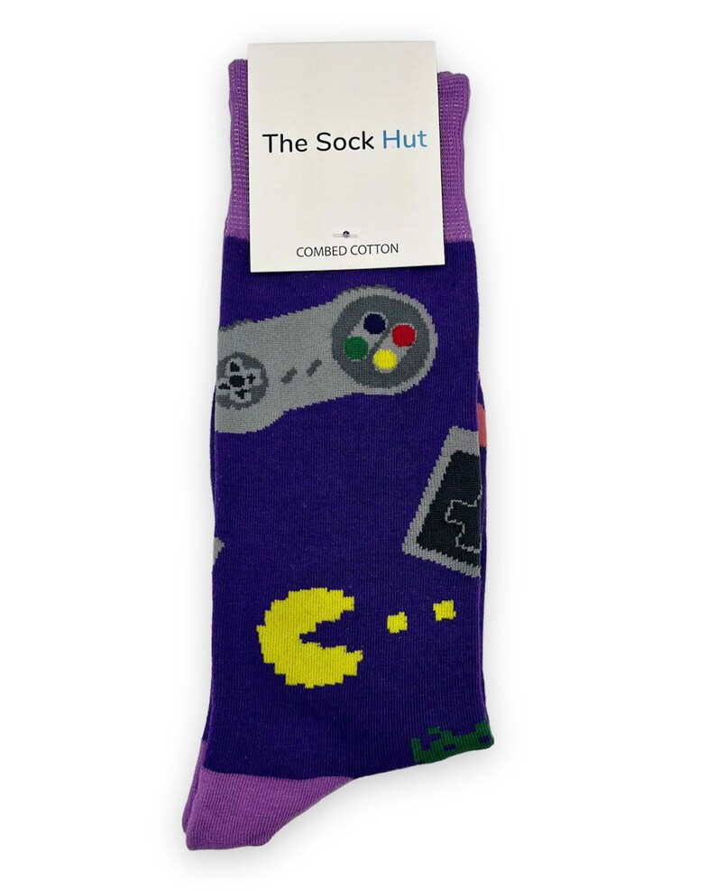 May include: Purple socks with a pattern of retro video game controllers, Pac-Man, and other pixelated graphics. The socks have a tag that says "The Sock Hut" and "Combed Cotton".
