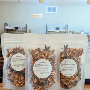May include: Three clear plastic bags filled with a blend of dried spices, including orange peel, cinnamon sticks, cloves, allspice, and star anise. The bags are labeled "Cauldron Spices" and list the ingredients. Each bag contains 3 ounces (85 grams) of spices.